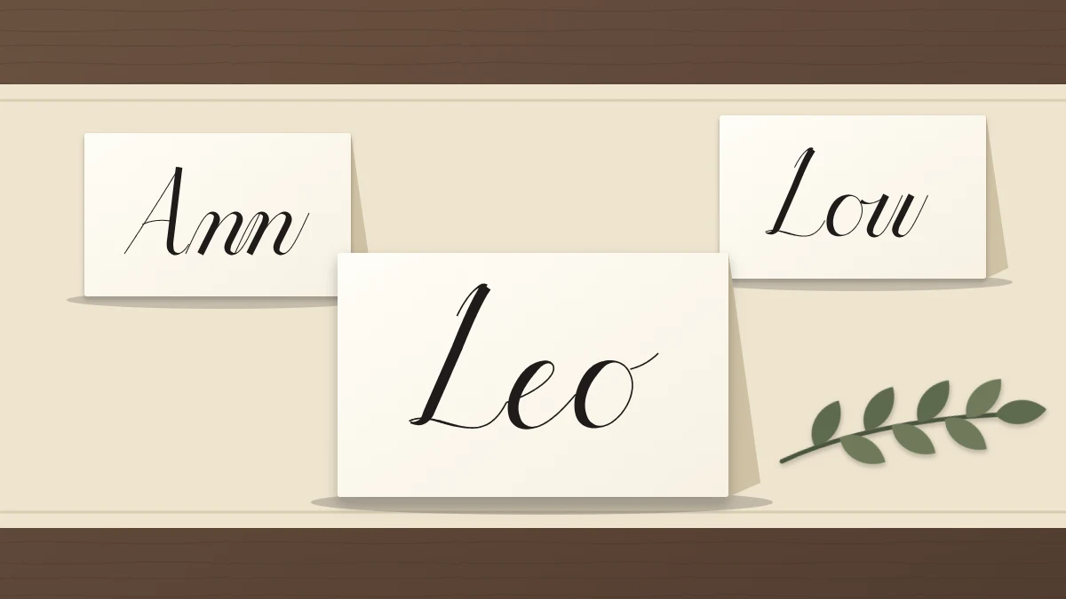 Three folded tent place cards with short names in script, the front one reading Leo, beside a small sprig of greenery