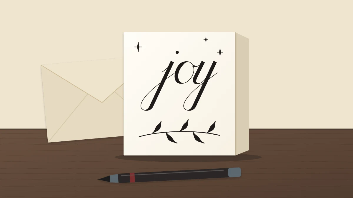 A folded ivory card with the word joy in script above a simple pen-stroke sprig, an envelope behind and a brush pen in front
